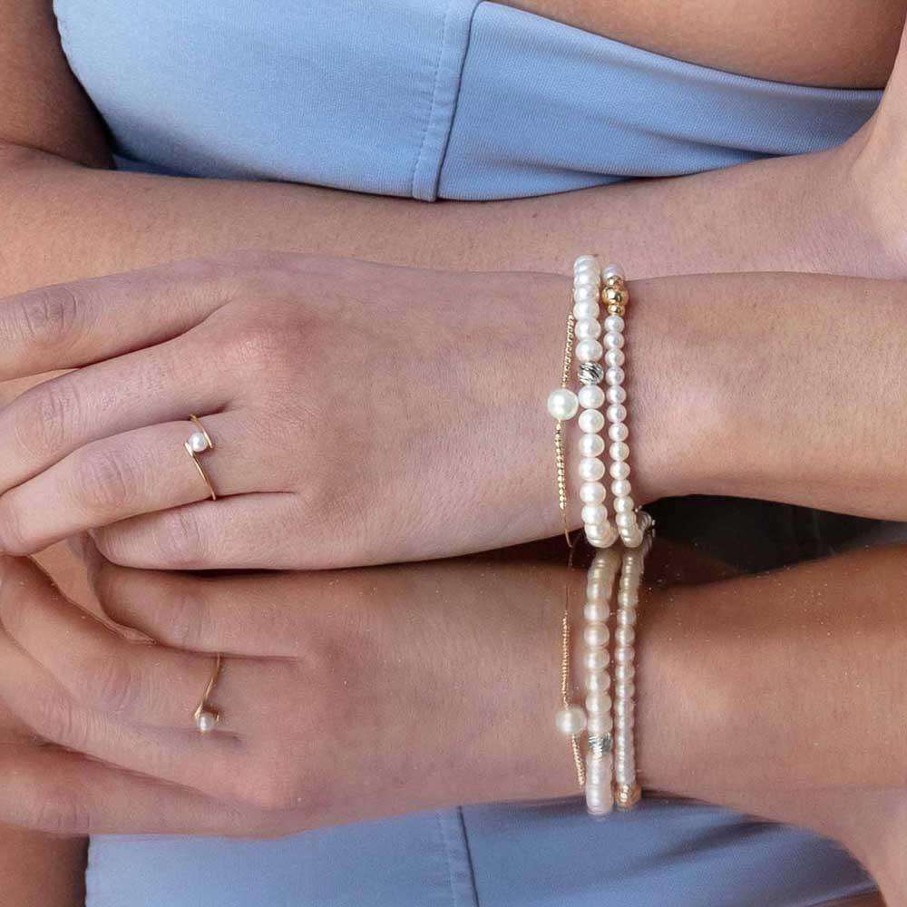 Polso con più bracciali di perle bianche e catenine dorate, anello sottile con perla