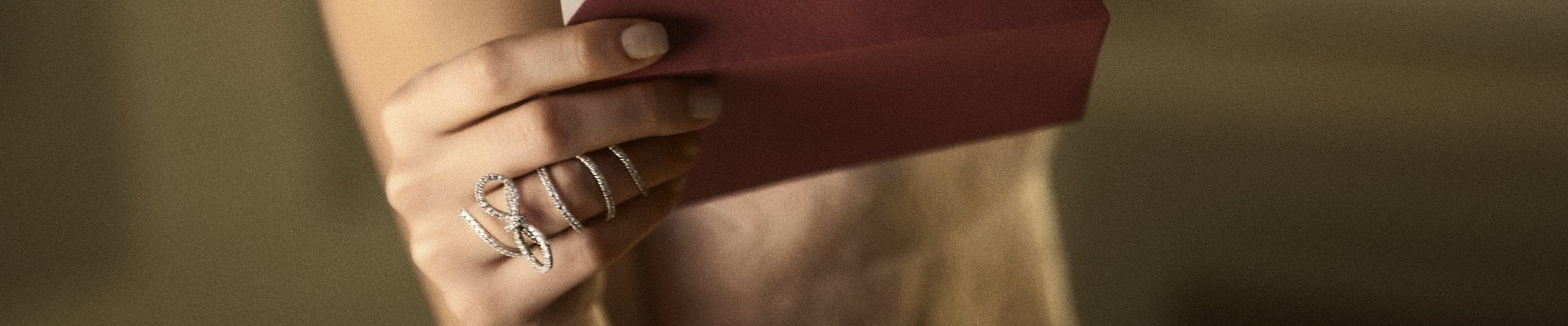Mano con anelli di diamanti che porge una busta bordeaux chiusa con sigillo di ceralacca